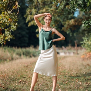 Beautiful brunette woman wearing ivory white silk slip skirt with a green silk camisole outdoors.