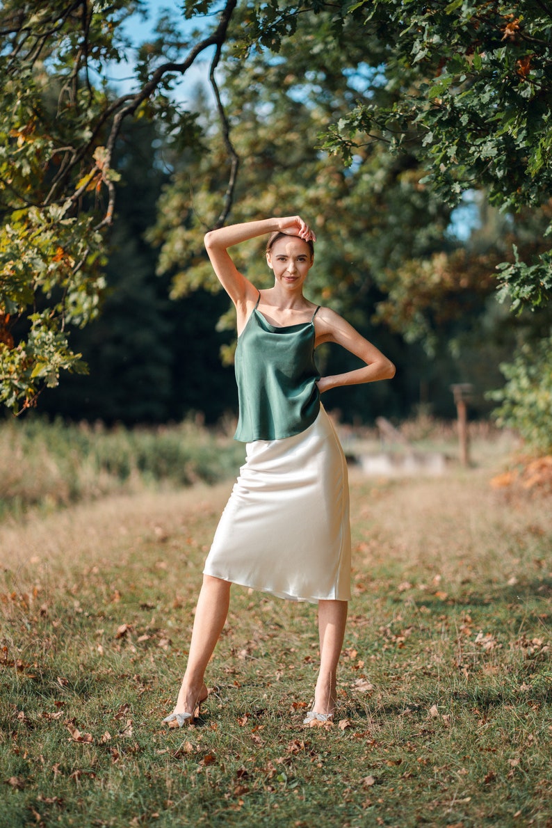 Beautiful brunette woman wearing ivory white silk slip skirt with a green silk camisole outdoors.