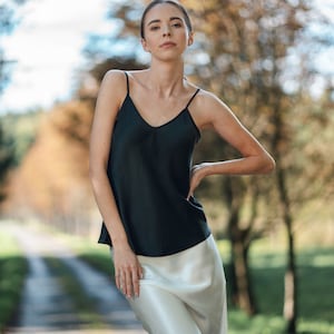 Beautiful brunette woman wearing ivory white silk slip skirt with a black silk camisole outdoors in nature. Hair tied up.