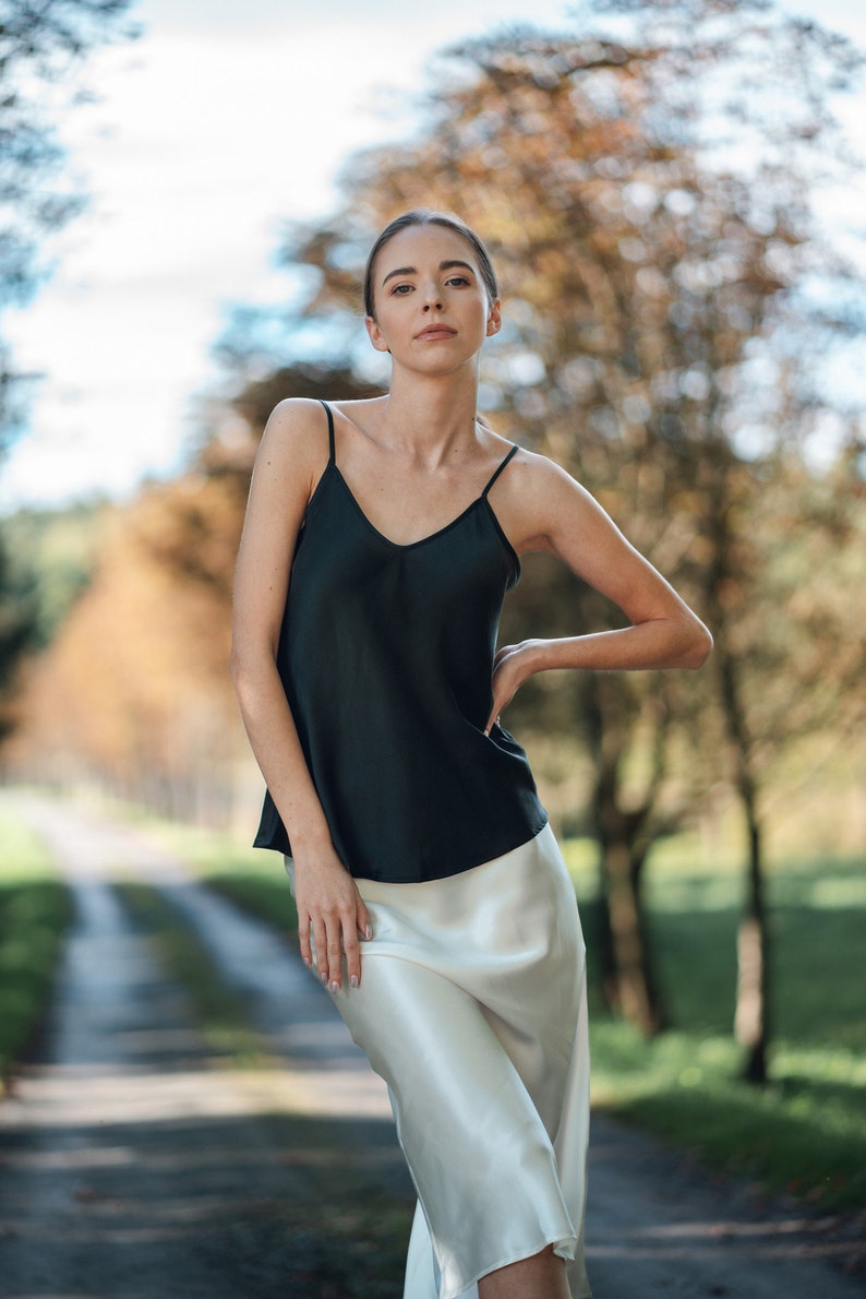 Beautiful brunette woman wearing ivory white silk slip skirt with a black silk camisole outdoors in nature. Hair tied up.