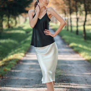 Beautiful brunette woman wearing ivory white silk slip skirt with a black silk camisole outdoors in nature on dirt road. Hair tied up.