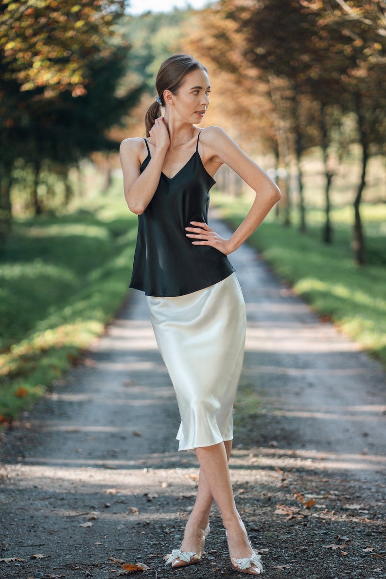 Beautiful brunette woman wearing ivory white silk slip skirt with a black silk camisole outdoors in nature on dirt road. Hair tied up.