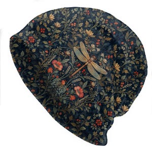 May include: A dark blue beanie featuring a detailed botanical print with red flowers, green leaves, and a prominent dragonfly centered on the fabric. The pattern includes small red berries and delicate stems spread across the entire surface of the hat.