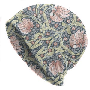 May include: A beanie hat with a floral pattern. The hat features large, stylized pink flowers, small orange flowers, and green leaves on a dark gray background. The design is reminiscent of vintage botanical illustrations.