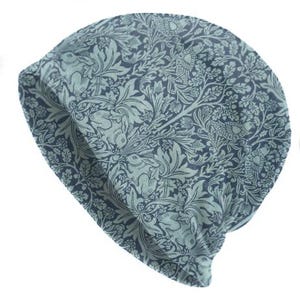 May include: A blue and green patterned beanie hat. The fabric features a repeating design of rabbits, birds, and foliage. The hat is made of a soft material and is suitable for casual wear. The hat is a stylish accessory.