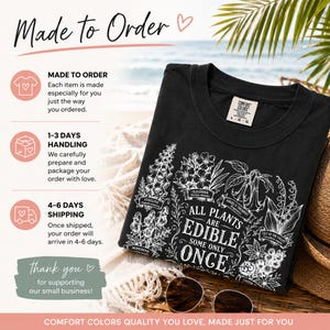 May include: A black t-shirt featuring a white botanical illustration of various plants including foxglove, oleander, angel's trumpet, lily of the valley, monkshood, and castor bean, with the text "ALL PLANTS ARE EDIBLE SOME ONLY ONCE".