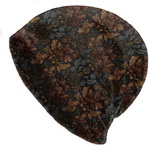 Puede incluir: Un gorro con un patrón repetido de hojas y bellotas de roble marrones, verdes y grises sobre un fondo azul oscuro. El gorro está hecho de un material suave y flexible, adecuado para el clima frío.
