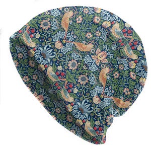 Könnte beinhalten: Eine dunkelblaue Beanie-Mütze mit einem sich wiederholenden Muster aus Vögeln, Blumen und Blättern in Grün-, Gelb- und Pfirsichtönen. Die Mütze besteht aus einem weichen, flexiblen Material und ist so konzipiert, dass sie eng am Kopf anliegt. Das Design hat einen Vintage- und botanischen Look.
