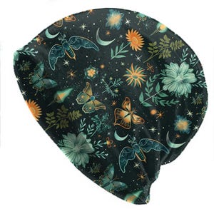 May include: A black beanie hat featuring a repeating pattern of butterflies, flowers, moons, and stars in teal, orange, and yellow. The hat is made of a soft material, suitable for all seasons.