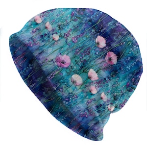 May include: A beanie hat with a watercolor floral design. The hat features a blue, teal, and purple background with pink poppies and lavender sprigs. The hat is a soft, comfortable accessory.