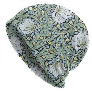 May include: A beanie hat with a floral pattern. The hat features a repeating design of white flowers, green leaves, and small yellow blossoms on a black background. The beanie is made of a soft, flexible material.