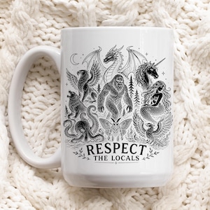 May include: A white ceramic mug featuring a detailed black ink illustration of various mythical creatures including a dragon, unicorn, mermaid, and bigfoot. The text "RESPECT THE LOCALS" is printed in a bold, black font at the bottom of the design.