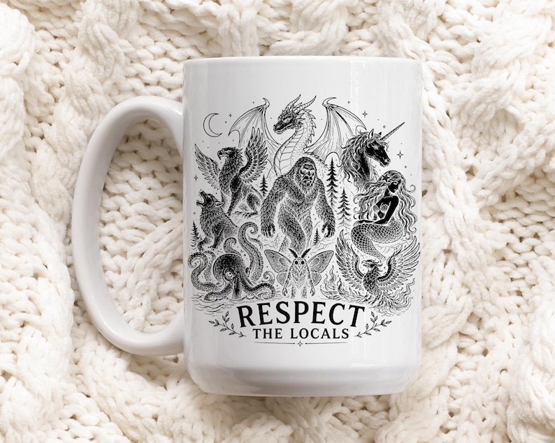 May include: A white ceramic mug featuring a detailed black ink illustration of various mythical creatures including a dragon, unicorn, mermaid, and bigfoot. The text "RESPECT THE LOCALS" is printed in a bold, black font at the bottom of the design.