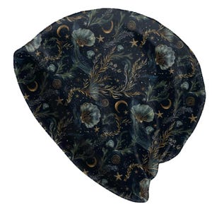 Könnte beinhalten: Eine dunkelblaue Beanie-Mütze mit einem Himmelsmuster. Das Design zeigt goldene und blaugrüne Muscheln, Halbmonde, Sterne und Blätterzweige. Die Mütze ist aus einem weichen, flexiblen Material gefertigt.