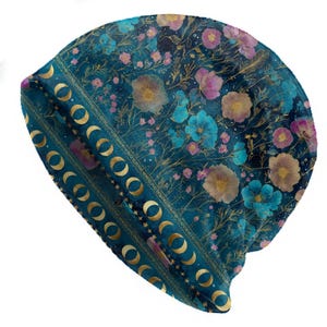 May include: A teal beanie hat with a floral pattern in shades of blue, pink, and gold. The hat features a band with gold crescent moon and star designs. The overall design is a whimsical, bohemian style.