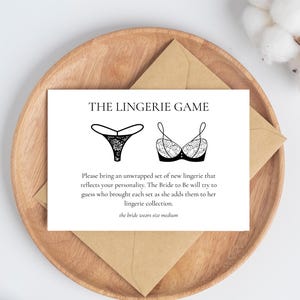 May include: A white card with the text "THE LINGERIE GAME" and instructions for a bridal shower game. The card features illustrations of lingerie and is placed on a wooden plate with a brown envelope.