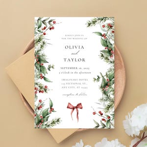 Può includere: Invito di nozze con i nomi Olivia e Taylor e dettagli dell'evento. Il design include fogliame verde, bacche rosse e un fiocco bordeaux. L'invito è su un piatto di legno con una busta beige.