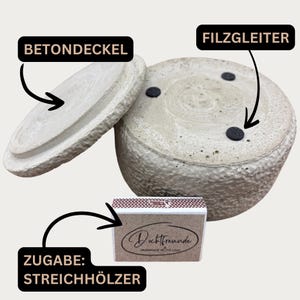 May include: A light gray concrete container with a matching lid and a box of matches. The container has a textured surface and three black felt pads on the bottom. The lid is slightly ajar, revealing the interior.