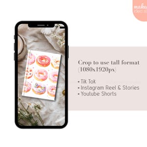 May include: A white notebook with a watercolor illustration of pink and white donuts on the cover. The notebook is sitting on a white fabric surface with a white flower.