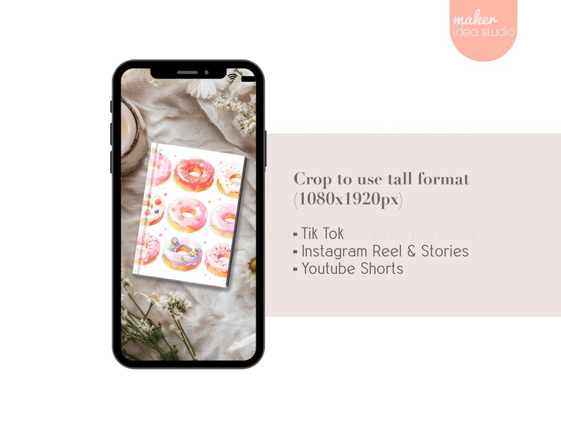 May include: A white notebook with a watercolor illustration of pink and white donuts on the cover. The notebook is sitting on a white fabric surface with a white flower.