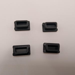 Puede incluir: Cuatro peque&ntilde;os componentes rectangulares negros de pl&aacute;stico est&aacute;n dispuestos sobre una superficie blanca. Cada componente tiene una abertura rectangular empotrada y un marco ligeramente elevado. Los componentes parecen estar impresos en 3D.