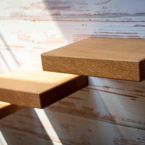 Könnte beinhalten: Drei Holzregale an einer weißen Wand montiert. Die Regale sind aus Naturholz mit einer hellbraunen Oberfläche. Die Regale sind versetzt, wobei das oberste Regal das größte und das unterste Regal das kleinste ist.