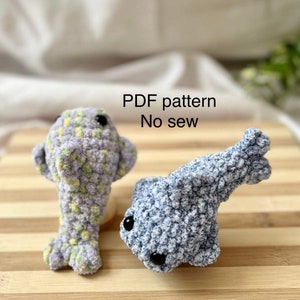 Può includere: Due peluche di delfino all'uncinetto, uno in colore lilla chiaro e giallo e l'altro in colore blu chiaro e bianco. Il testo "PDF pattern No sew" è scritto sopra i peluche.