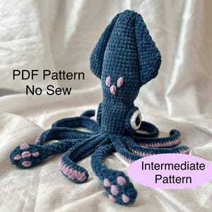 May include: A handmade, blue crochet squid with pink detailing. The squid features large eyes and multiple tentacles. The image includes the text "PDF Pattern No Sew" and "Intermediate Pattern".