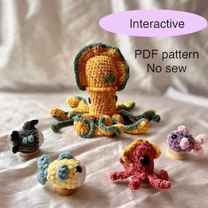 May include: A set of five crocheted sea creatures, including a squid, a pufferfish, a fish, and two octopuses. The squid is yellow and green, the pufferfish is black and white, the fish is yellow and blue, and the octopuses are pink and purple. The text "Interactive PDF pattern No sew" is visible in the image.