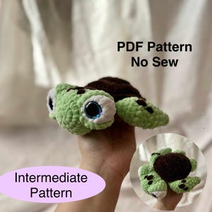 以下が含まれることがあります： 薄緑色の体、茶色の甲羅、大きな青い目をしたかぎ針編みのカメ。画像には「PDF Pattern No Sew」と「Intermediate Pattern」というテキストが含まれています。