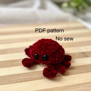 Puede incluir: Un juguete de amigurumi de cangrejo de crochet rojo con ojos negros. El juguete está sobre una superficie de madera. Patrón PDF. Sin coser.