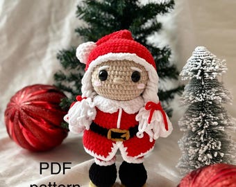 Puede incluir: Una muñeca de Papá Noel tejida a ganchillo con gorro rojo y pompón blanco, abrigo rojo con ribete blanco, cinturón negro con hebilla dorada y botas negras. La muñeca tiene cara beige con ojos negros y mejillas rosadas. Texto PDF pattern.