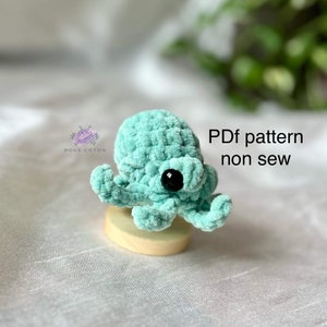 May include: A crocheted turquoise octopus with black eyes. The octopus is sitting on a wooden base. The text "PDF pattern non sew" is visible in the image.