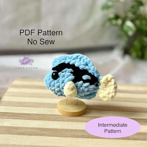 May include: A crocheted blue and black fish with white fins. The fish is on a wooden stand. The text "PDF Pattern No Sew" and "Intermediate Pattern" is visible in the image.