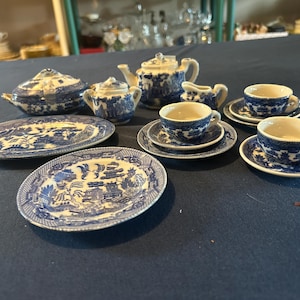 May include: A miniature blue and white porcelain tea set. The set includes a teapot, sugar bowl, creamer, serving dishes, and several teacups with saucers. The design features a classic landscape pattern.