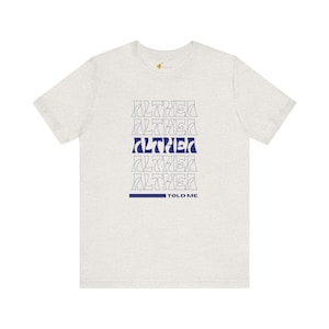 Puede incluir: Una camiseta gris jaspeada con un gráfico azul marino que dice "ALTHEA" repetido cinco veces. El texto está en una fuente estilizada. Debajo del gráfico, dice "TOLD ME" en una fuente más pequeña.