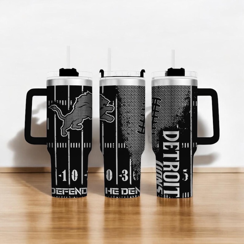 Puede incluir: Tres vasos de los Detroit Lions en blanco y negro con asas. Cada vaso presenta el logotipo del equipo, las l&iacute;neas del campo de f&uacute;tbol y las palabras "DEFEND", "THE DEN" y "DETROIT LIONS". Los vasos tienen un asa negra y una pajita blanca.
