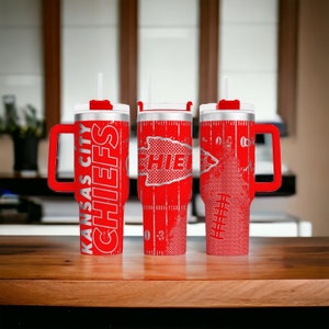 K&ouml;nnte beinhalten: Drei rote isolierte Becher mit wei&szlig;en Deckeln und Griffen. Die Becher zeigen die Worte "KANSAS CITY CHIEFS" und ein Football-Design. Jeder Becher hat einen wei&szlig;en Strohhalm.