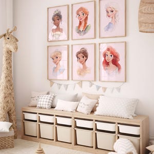 May include: Six framed prints of Disney princesses, including Tiana, Ariel, Cinderella, Rapunzel, Elsa, and Belle, are displayed on a white wall above a wooden storage bench with white drawers.