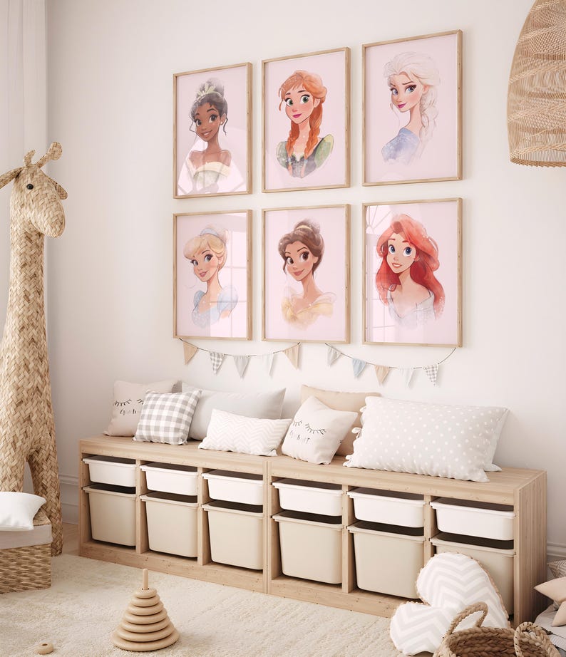 May include: Six framed prints of Disney princesses, including Tiana, Ariel, Cinderella, Rapunzel, Elsa, and Belle, are displayed on a white wall above a wooden storage bench with white drawers.