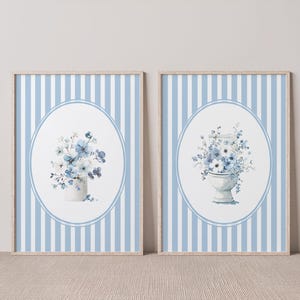 May include: Two framed prints with blue and white striped backgrounds. One print features a vase of blue flowers, the other a toilet with blue flowers. Both are set within an oval frame.