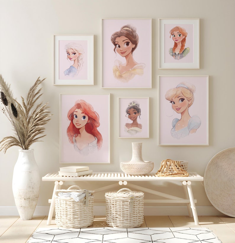 May include: A white wall with a collection of framed illustrations of Disney princesses. The princesses include Ariel, Belle, Cinderella, Tiana, Elsa, and Rapunzel. The frames are white and the illustrations are on a pink background. The frames are arranged in a grid pattern on the wall. There is a white bench with two white wicker baskets underneath. There is a white vase with dried flowers on the left side of the image. There is a white wicker tray with a wooden bowl and a beaded necklace on the bench.