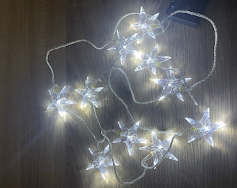 May include: A string of white LED fairy lights with clear star-shaped bulbs. The lights are strung together with a clear wire and are arranged in a random pattern.
