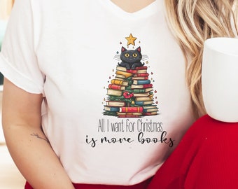 Op de afbeelding: Wit T-shirt met een zwarte kat die op een stapel boeken zit die de vorm van een kerstboom heeft. De tekst luidt "Alles wat ik voor kerst wil, zijn meer boeken".