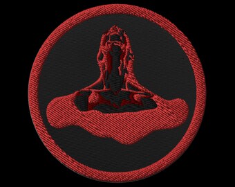 May include: Embroidered patch featuring a stylized red figure within a black circle. The figure appears to be in a seated position, with a detailed outline. The patch has a red border and is set against a black background.