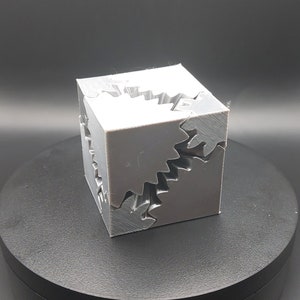 May include: A grey 3D printed cube with interlocking gears on each side.