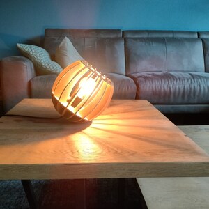 Peut inclure: Une lampe en bois avec un design géométrique est posée sur une table en bois. La lampe est allumée et projette une lueur chaude sur la table.