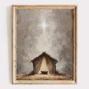 May include: A framed painting of a nativity scene. A bright star shines above a rustic stable with a thatched roof and a draped interior. The artwork uses a muted colour palette of browns, tans, and greys, creating a serene and reverent atmosphere.