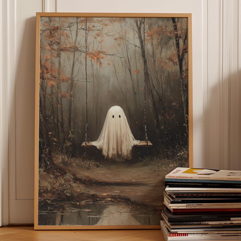 Op de afbeelding: Een ingelijste muurkunstprint met een witte spookfiguur gehuld in een laken, zittend op een houten schommel die aan kettingen hangt in een donker, mistig bos met bruine herfstbladeren en een kleine plas water die het tafereel weerspiegelt.