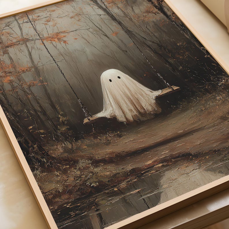Op de afbeelding: Een ingelijste muurkunstprint met een witte geestfiguur met twee zwarte ogen die op een houten schommel zit, opgehangen aan kettingen. De sc&egrave;ne speelt zich af in een donker, sfeervol bos met bruine en grijze tinten, kale bomen en bladeren.